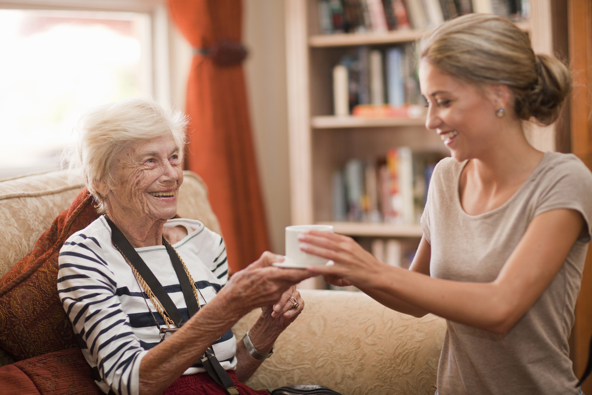 An in-home caregiver handing a cup to a senior